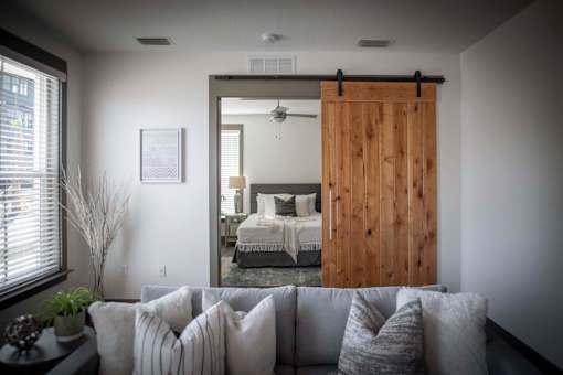A bedroom with a bed and a mirror is visible through a wooden door.