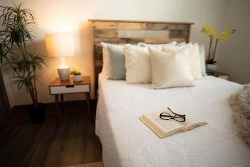 A bed with white pillows and a book with glasses on top of it.