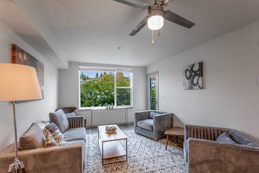 A living room with a brown couch, a grey armchair, a coffee table, and a ceiling fan.