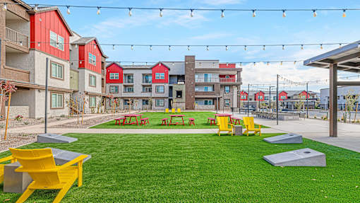 A grassy area with picnic tables and benches in front of apartment buildings.