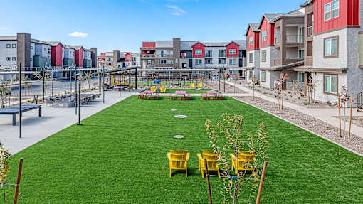A grassy area with yellow chairs and a playground in the background.