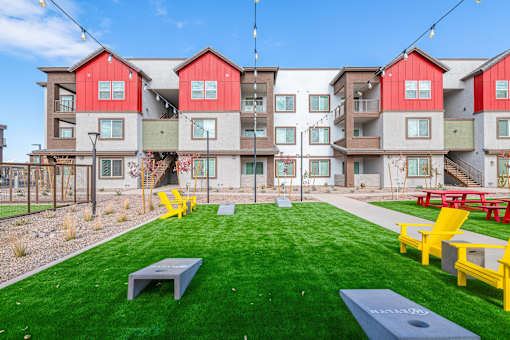 A grassy area in front of apartment buildings with yellow chairs and tables.