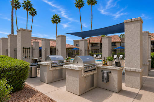 A row of outdoor BBQs are lined up under a blue shade sail.