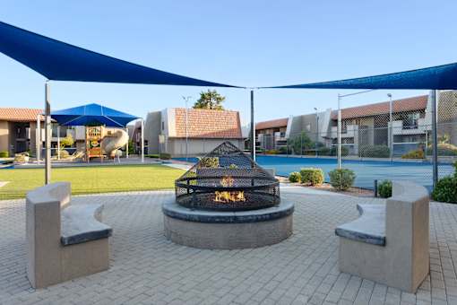 A fire pit is surrounded by two concrete benches under a blue canopy at Denim Scottsdale, Scottsdale, AZ