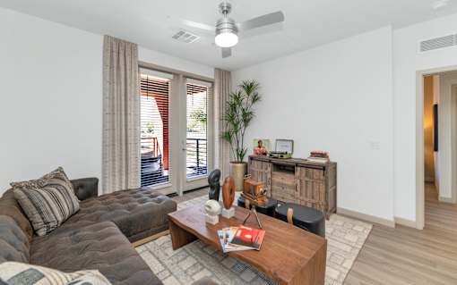 A living room with a brown leather couch, a wooden coffee table, and a ceiling fan.