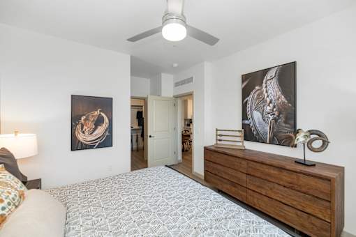A bedroom with a bed, a ceiling fan, and two paintings on the wall.