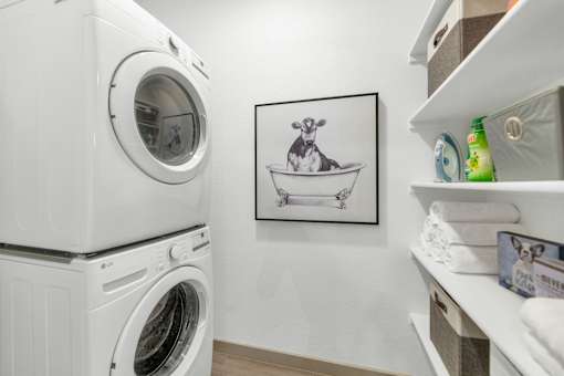 A laundry room with a washing machine and a shelf with towels and detergent.