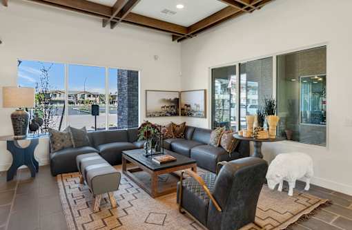 A living room with a black leather couch and a white sheep toy on the carpet.