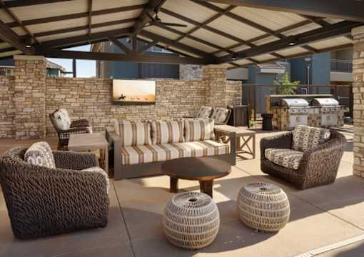 A patio with a couch, chairs, and tables under a roof.