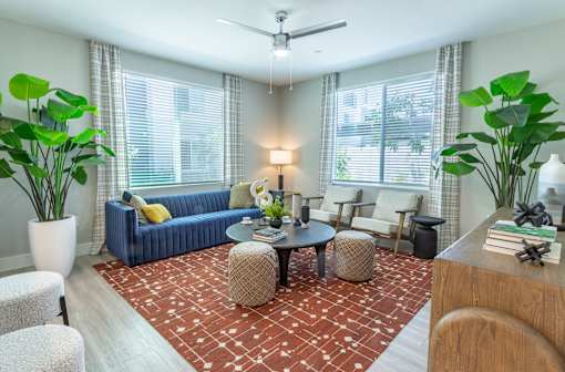 A living room with a blue couch, a red patterned rug, and a ceiling fan.