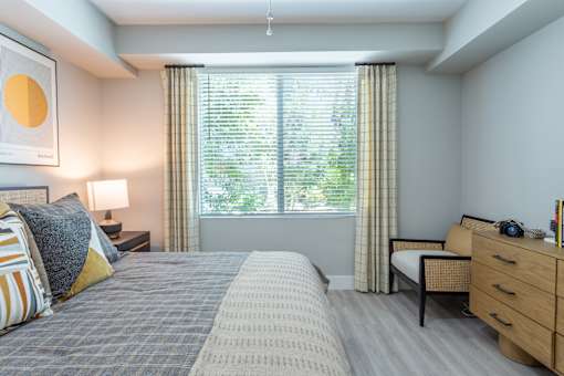 A bedroom with a large bed, a nightstand, and a window with curtains.