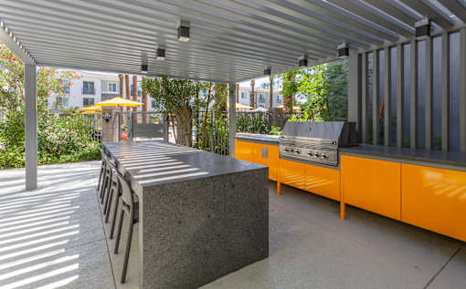 A grey concrete bench with a metal frame is in the foreground of a sunny outdoor area.