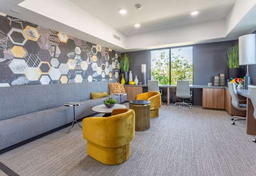 A modern office space with a grey sofa, yellow chairs, and a patterned wallpaper.