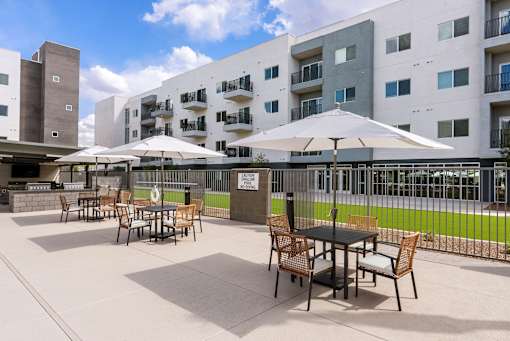 Outdoor patio with dining tables and umbrellas at Lucero Apartments, Phoenix, 85051