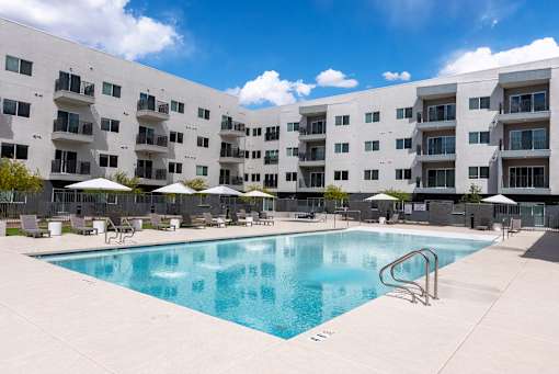 Swimming pool with lounge chairs and umbrellas at Lucero Apartments, Phoenix, Arizona