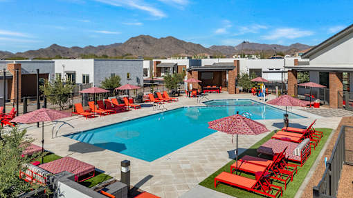 A pool surrounded by red chairs and umbrellas.at Marketside Villas at Verrado, Buckeye, AZ