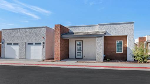 A modern house with a grey and brown facade and a red brick chimney.at Marketside Villas at Verrado, Buckeye, AZ