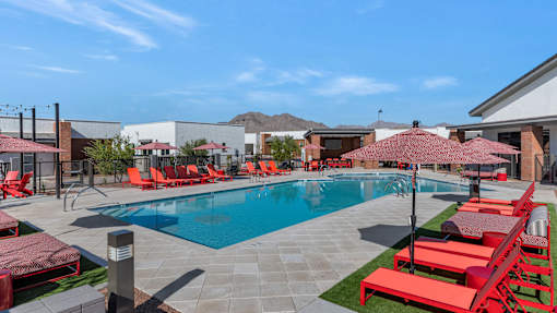 A pool surrounded by red chairs and umbrellas.at Marketside Villas at Verrado, Buckeye, 85396