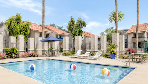 A pool with a blue umbrella and four beach balls.