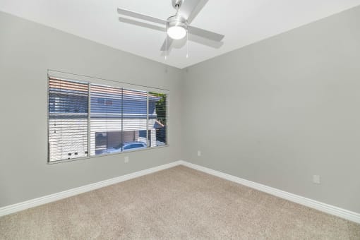 an empty bedroom with a large window and a ceiling fan