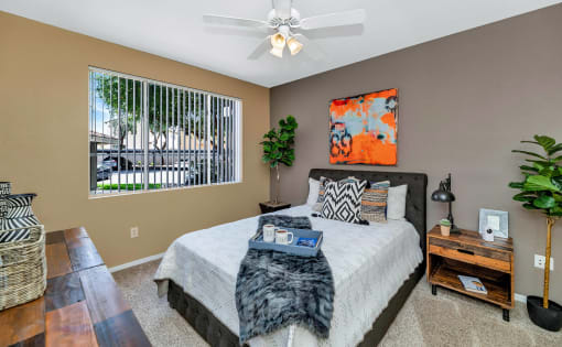 A bedroom with a large bed, a ceiling fan, and a window with blinds at Montage at Pecos Ranch Apartments, Arizona