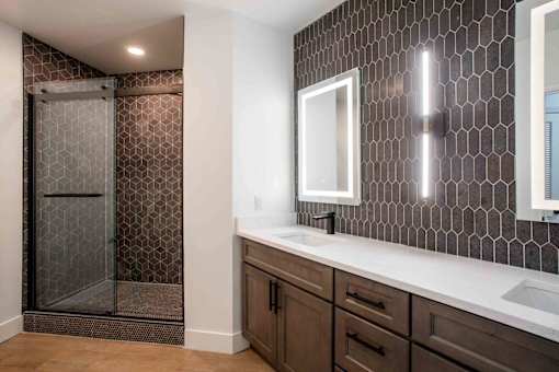 A bathroom with a brown tile shower and a white sink. at The Laurel Apartments, Arizona  