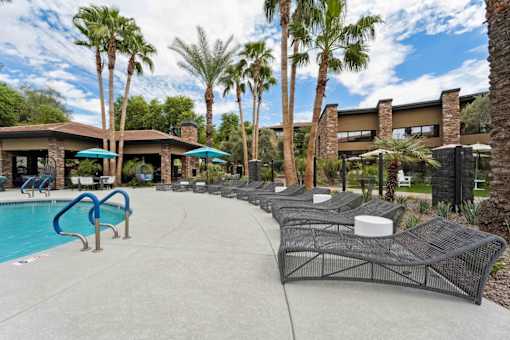 A pool area with a blue pool, lounge chairs, and palm trees. at The Laurel Apartments, Chandler, AZ  