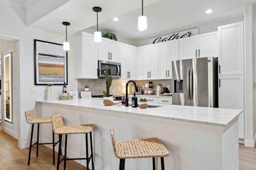 A kitchen with white cabinets and a white island with two barstools. at The Laurel Apartments, Arizona  