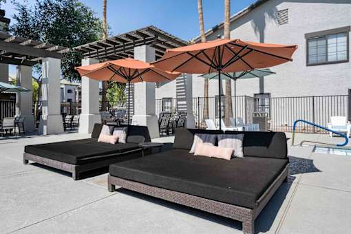 Two cushioned daybeds are placed under umbrellas on a patio. at Lazo Apartment Homes, Chandler, AZ  