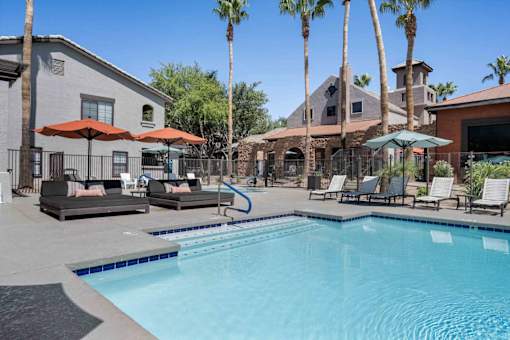 A pool surrounded by palm trees and lounge chairs. at Lazo Apartment Homes, Chandler  