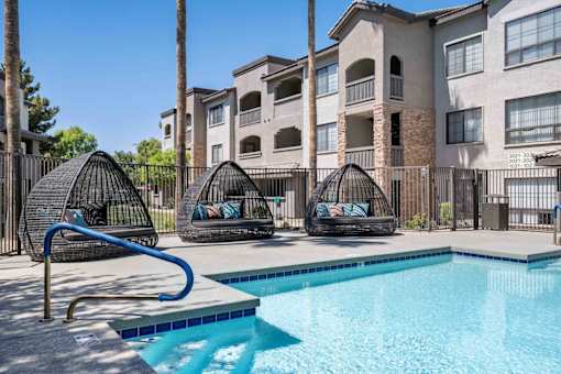 A swimming pool with a slide and two hanging chairs in front of apartment buildings. at Lazo Apartment Homes, Chandler, AZ 85225  