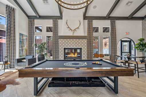 A pool table is in the middle of a room with a fireplace and a deer head mounted on the wall. at Lazo Apartment Homes, Chandler, AZ  