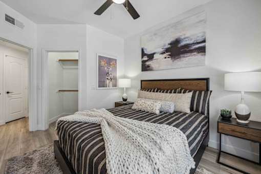 A bedroom with a bed, two lamps, and a painting on the wall. at Lazo Apartment Homes, Arizona  