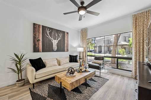 A living room with a white couch, a wooden coffee table, and a deer head picture on the wall. at Lazo Apartment Homes, Chandler Arizona  