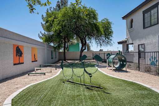 A playground with a swing set and a tree in the middle of a grassy area. at Lazo Apartment Homes, Chandler Arizona  