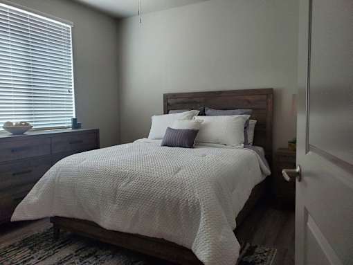 Bedroom with wooden furniture and white bedding at Pinon Lofts Apartments, Arizona