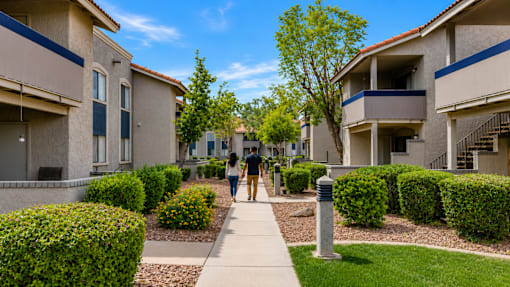 Two people walking down a sidewalk between two buildings.