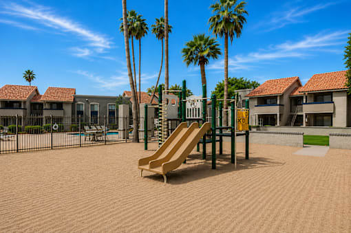 A playground with a slide, palm trees, and a swimming pool in the background.
