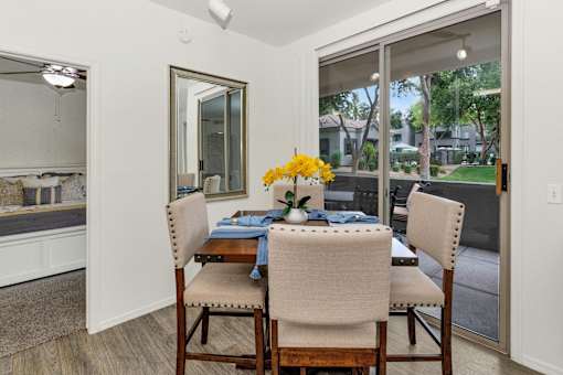 A dining room with a table set for two and a view of a residential area outside the window.