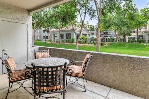 A patio with a table and chairs overlooking a grassy area.