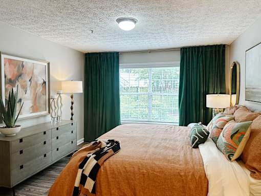 A bedroom with a bed, dresser, and window with green curtains.
