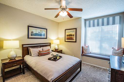 A bedroom with a bed, nightstand, and window seat.