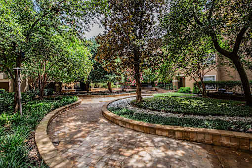 A curved brick pathway leads through a landscaped area with trees and shrubs.