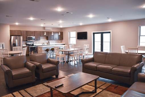 A living room with brown leather furniture and a kitchen in the background.