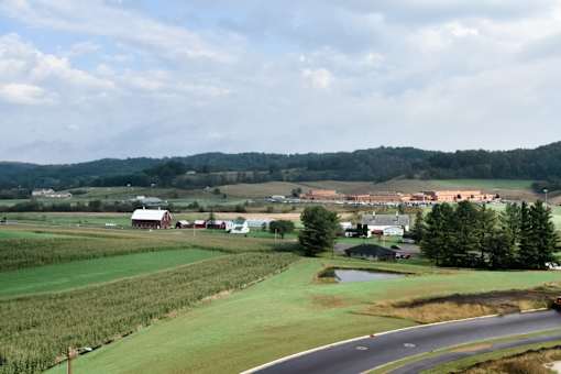 A road with a curve in the foreground with a farm in the background.