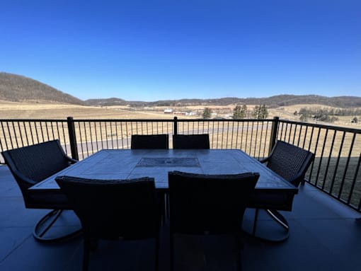 A table with chairs is set up on a balcony with a view of the countryside.
