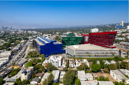 A large building with a red and green section is in the foreground of a cityscape.