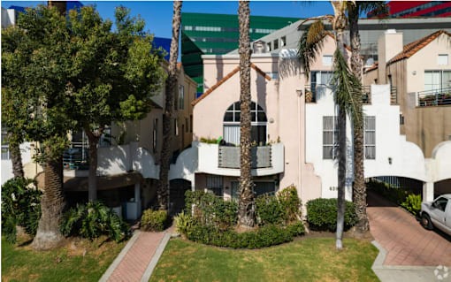 A white building with a balcony is surrounded by greenery.