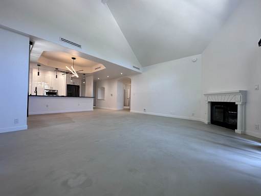 A large, empty room with a fireplace and a kitchen area in the background.