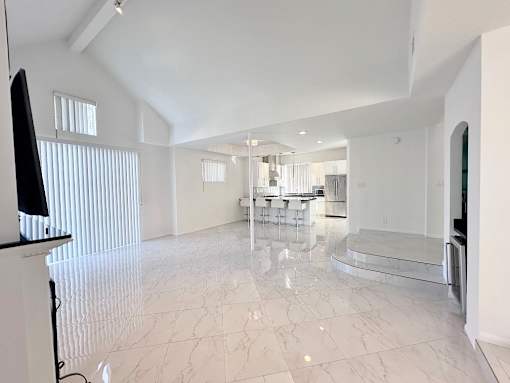 A spacious living room with a television and a dining area in the background.